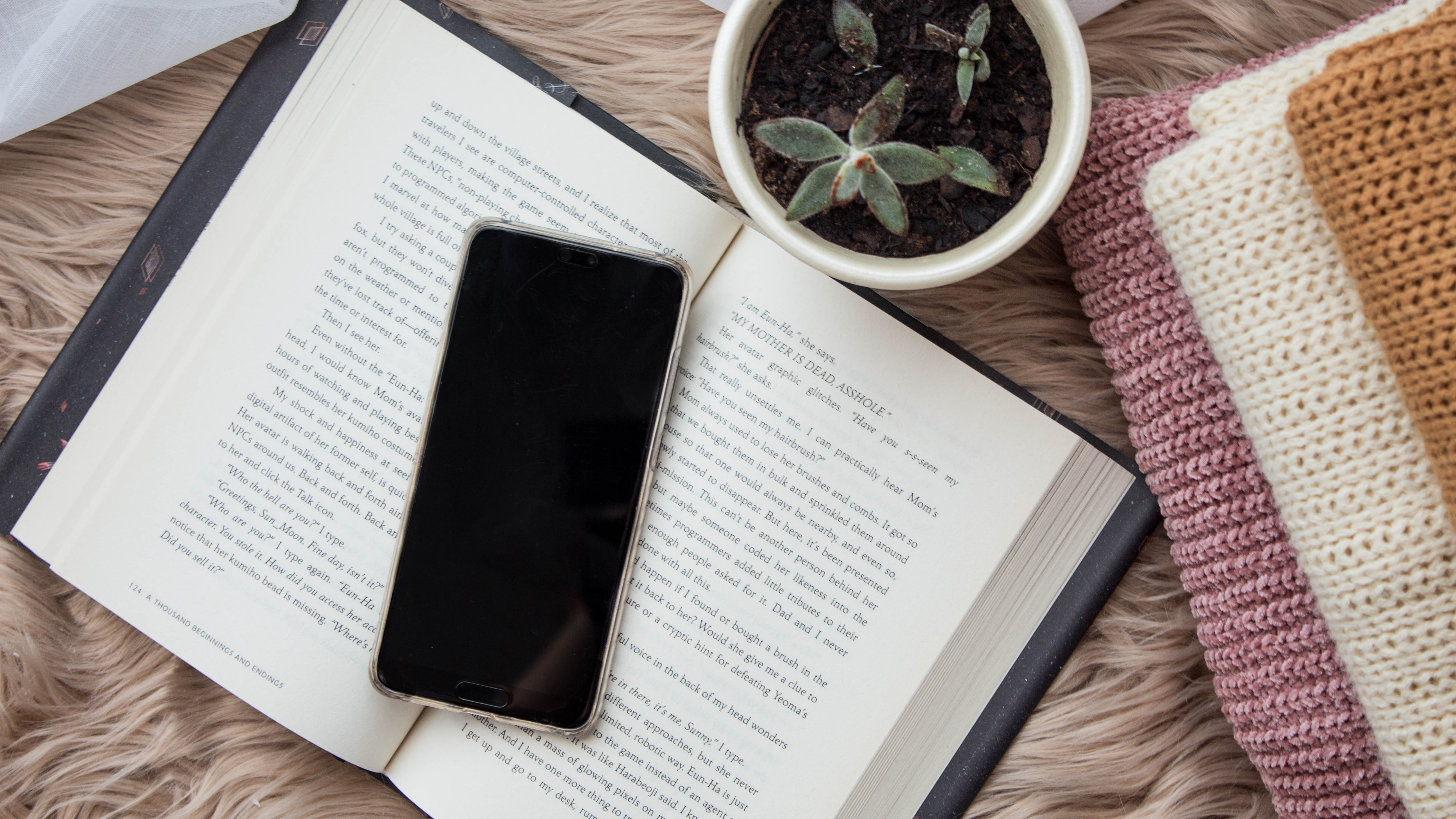 Open book next to a stack of knitted sweaters.