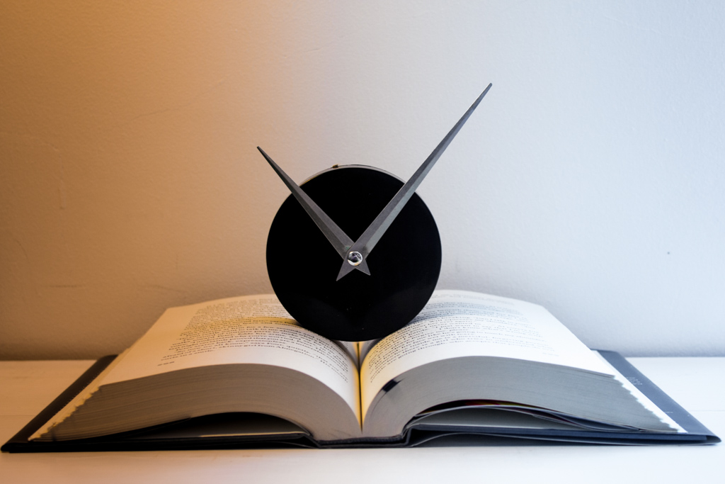 Illustrated image of an open book with a clock on top with a gradiant from left to right going from sepia to white.