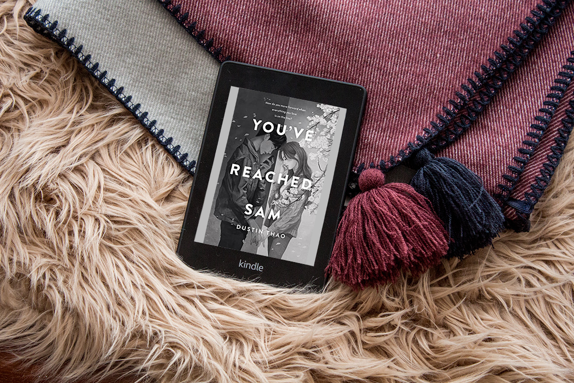 Flatlay of the Kindle displaying the book cover on top of a cosy scarf.