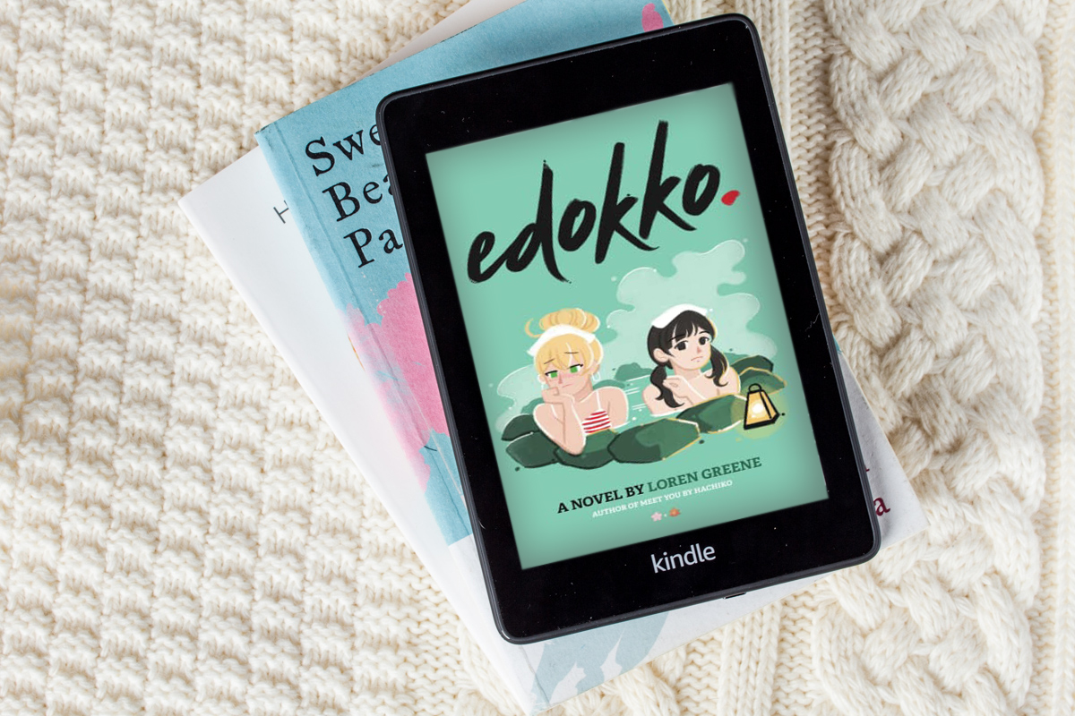 Flatlay of a small stack of books with a Kindle with a fullcolouredimage of "Edokko" cover.