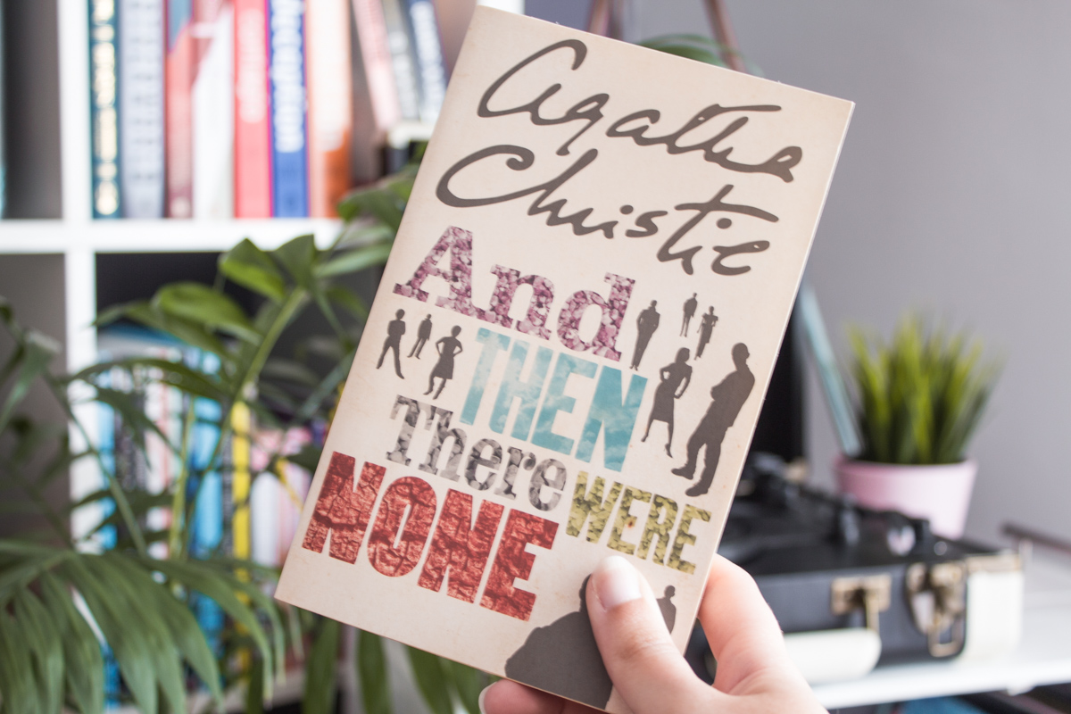 Holding the book with a bookshelf in the background.