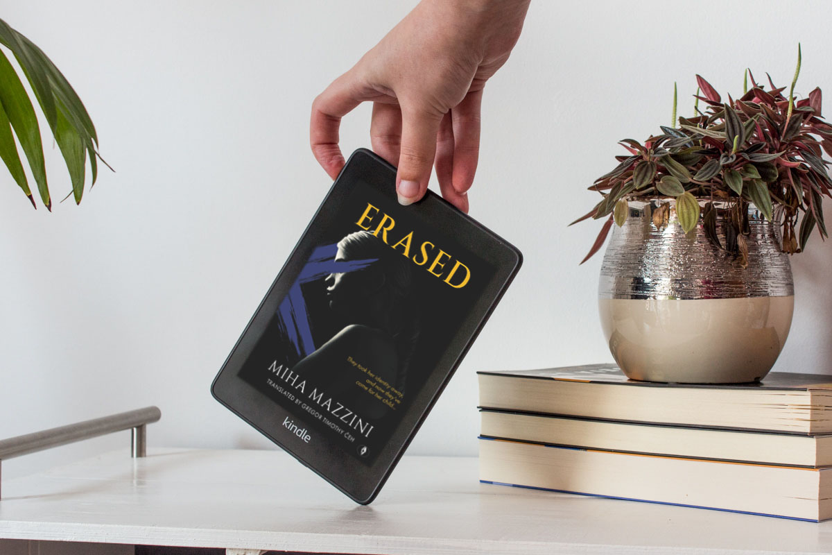 Holding a Kindle showing the full-colour cover of Erased.
