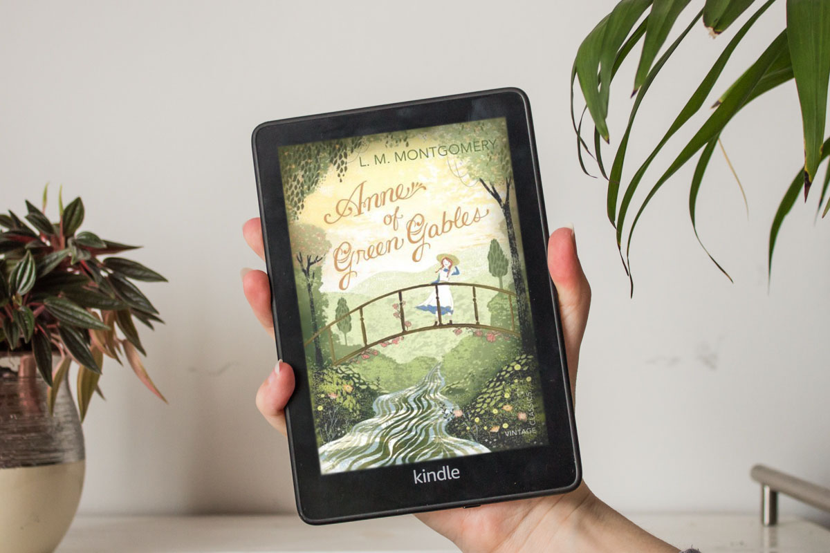 Holding a Kindle with the coloured cover of Anne of Green Gables.