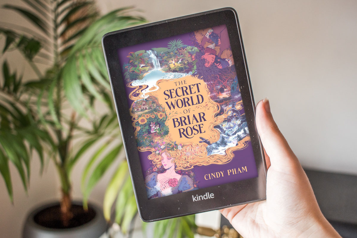 One hand holding a kindle showing the coloured cover of The Secret World of Briar Rose.
