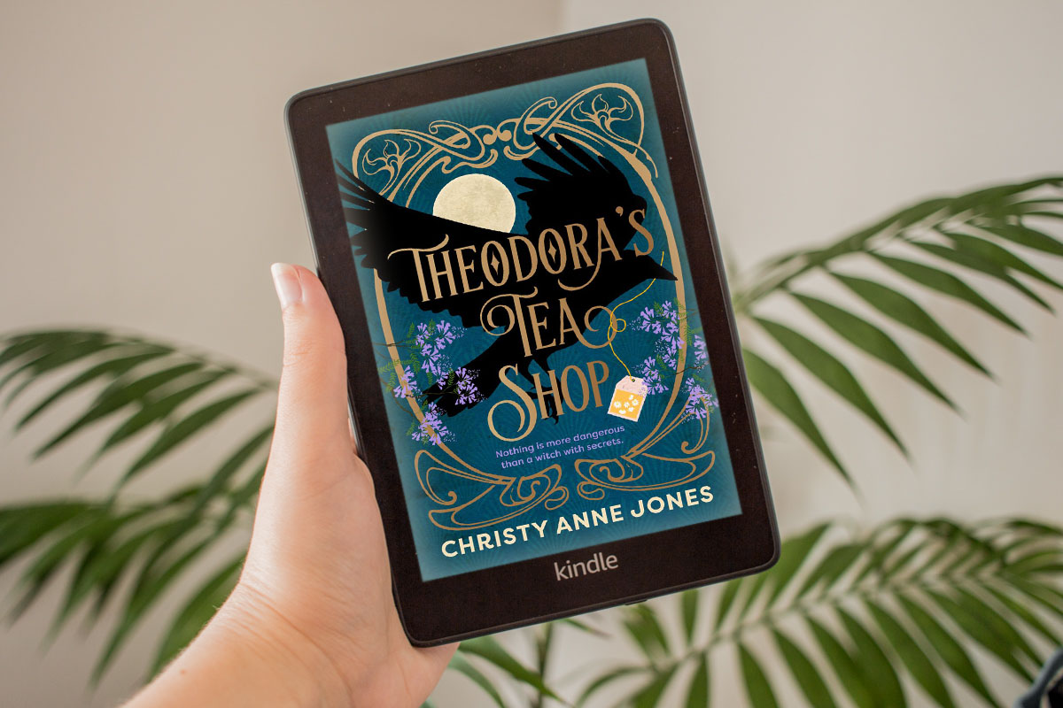 Holding a Kindle with the coloured cover of Theodora's Tea Shop.